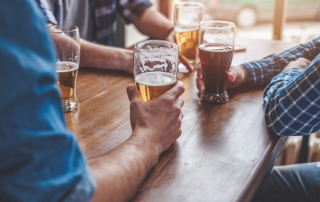 Close up of men holding beers on a table.